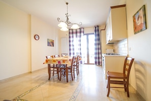 A dining area with a table set for four, a kitchen with a stove and cabinets, and a clock on the wall. - Sea-View Etna Residence (Trecastagn)