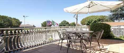An outdoor patio with a table and chairs, a white umbrella, and flags in the background.