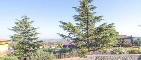 A residential area with stone walls, a paved walkway, and a view of houses and greenery in the distance.