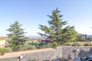 A residential area with stone walls, a paved walkway, and a view of houses and greenery in the distance. - Sea-View Etna Residence (Trecastagn)