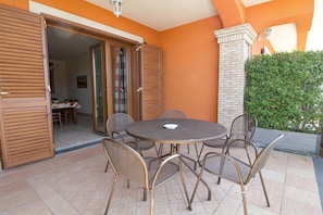 An outdoor patio with a round table and six chairs, a sliding glass door leading to an interior dining area, and a brick pillar with a light fixture. - Sea-View Etna Residence (Trecastagn)