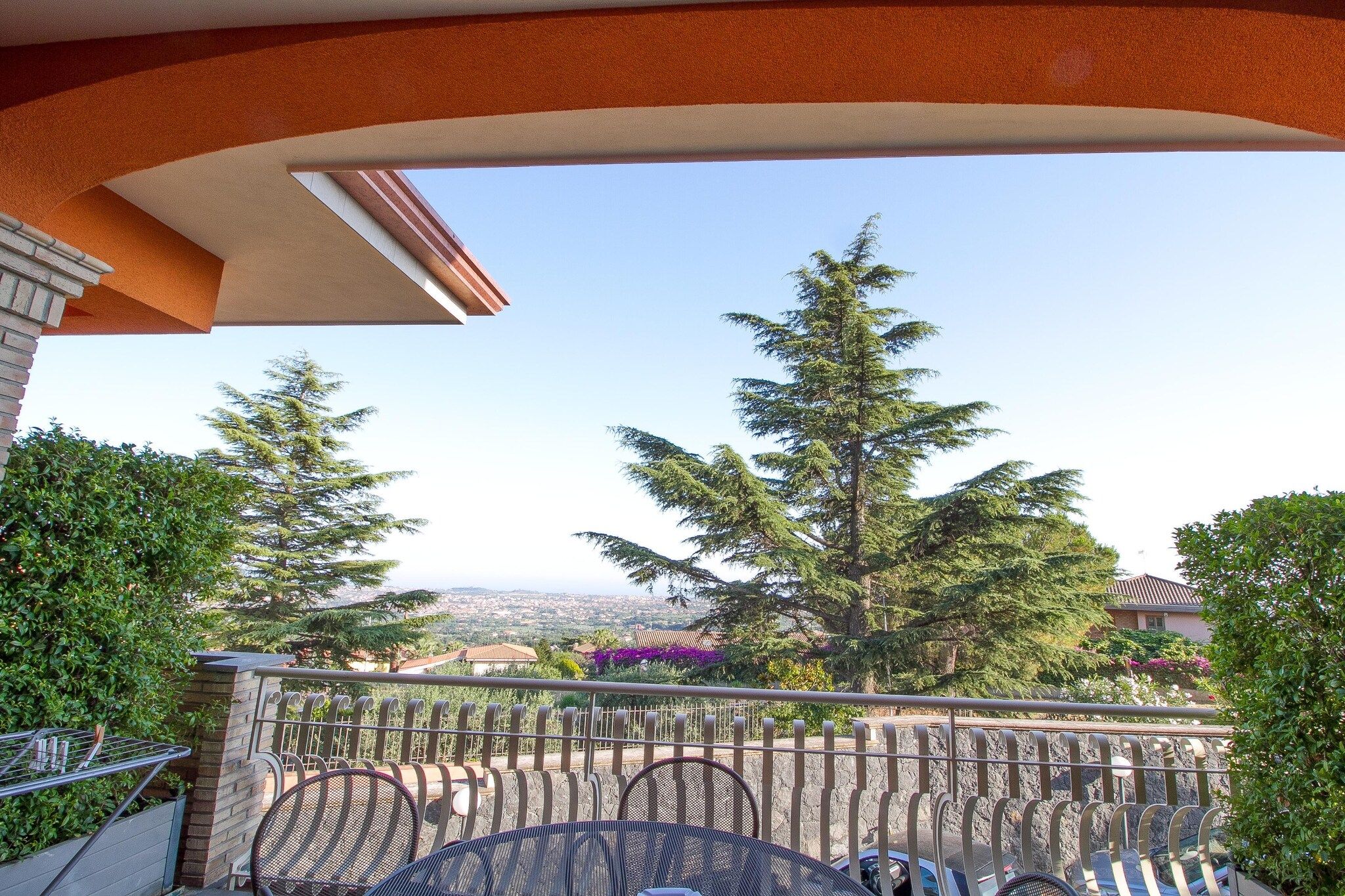 Un balcon offrant une vue sur le paysage urbain, les arbres et un ciel dégagé.