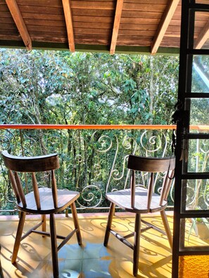 Two wooden chairs on a tiled patio with a metal railing, overlooking a lush garden. - House for 10 in an oak Forest Santa Elena (Medellín)