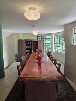 A dining room with a long wooden table, chairs, a chandelier, and a view through large windows. - House for 10 in an oak Forest Santa Elena (Medellín)