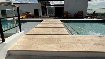 Zona de piscina con escalones que conducen a un edificio, cielo despejado y vista al mar.