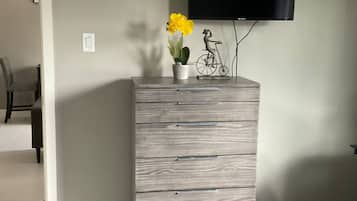 A room with a grey dresser, a flat-screen TV mounted on the wall, and a potted plant with yellow flowers on top.