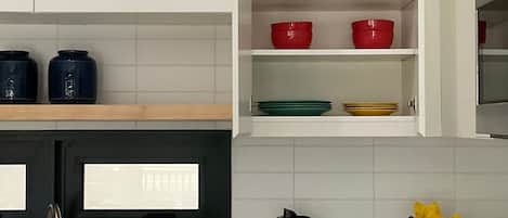 A modern kitchen with white cabinets, a stainless steel sink, a blender, and a potted plant.