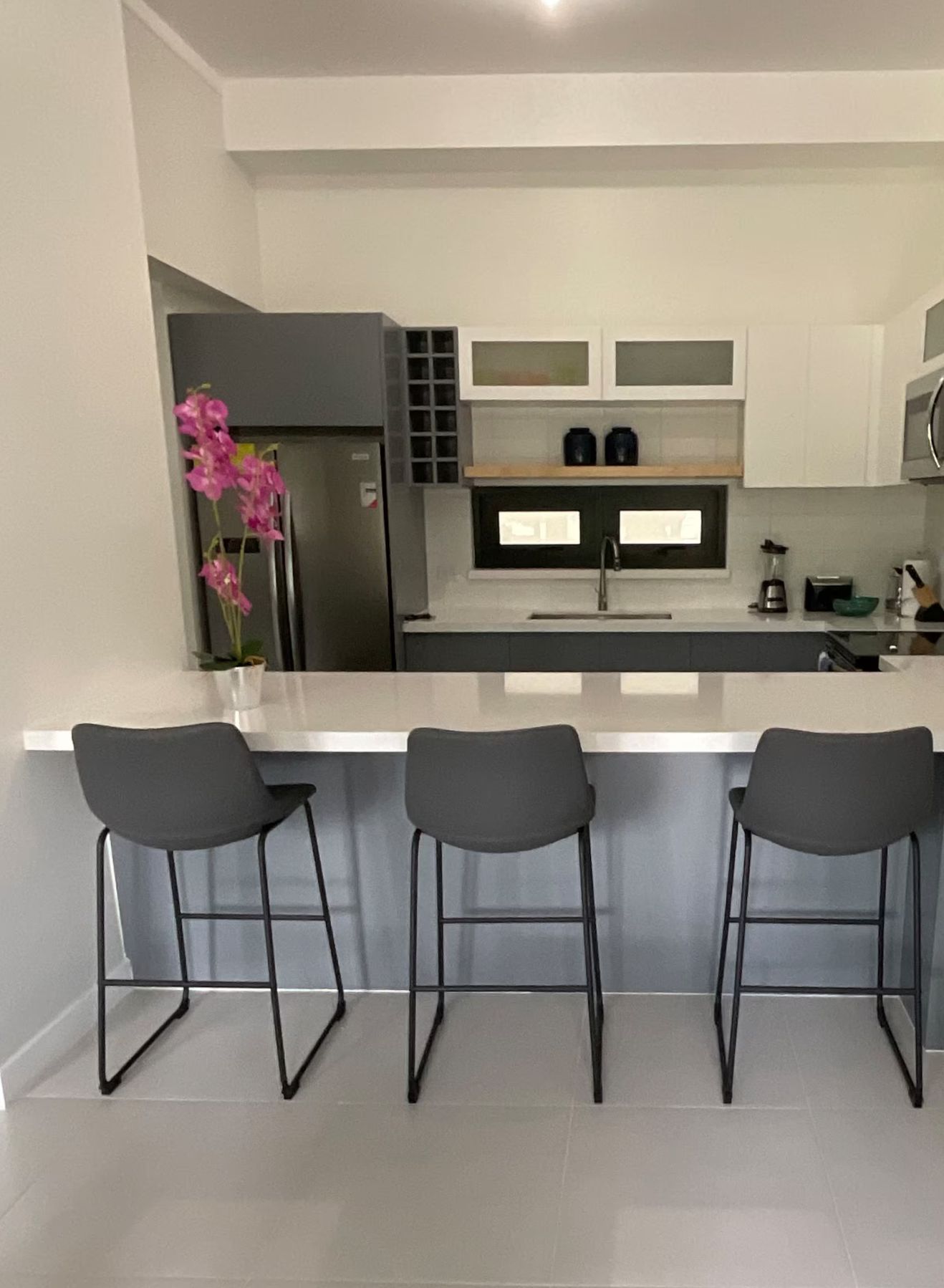 A modern kitchen with a central island, three bar stools, and a refrigerator.