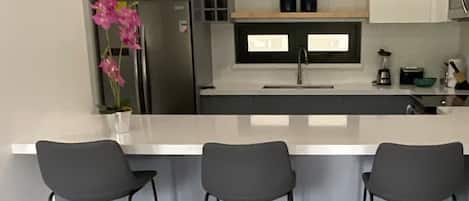 A modern kitchen with a central island, three bar stools, and a refrigerator.