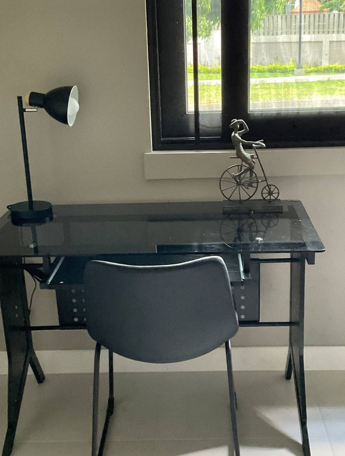 Ett rum med ett skrivbord, en stol, en lampa och ett fönster med utsikt över grönområden.