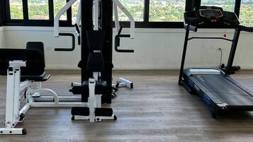 Un gimnasio con cinta de correr y máquina Body-Solid, amplias ventanas con vistas a montañas y suelo de madera.
