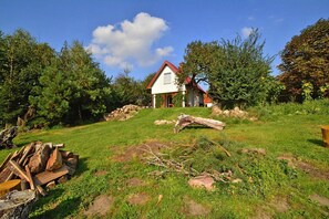 A house with a red roof, surrounded by a grassy area with trees and a pile of firewood.