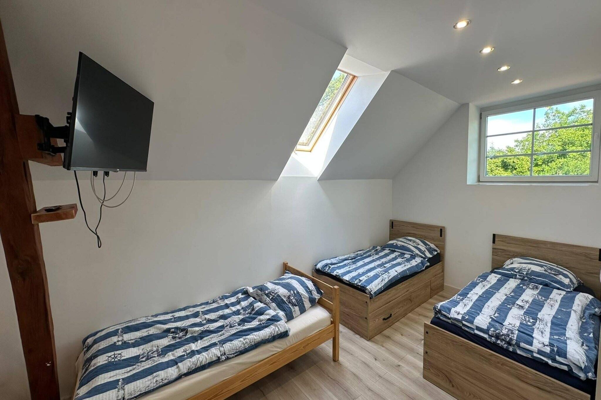 Une chambre à coucher avec deux lits en bois, un téléviseur fixé au mur et une lucarne.
