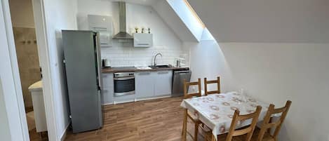 Une cuisine compacte avec un coin repas, comprenant une table et des chaises en bois, un four encastré et un petit évier.