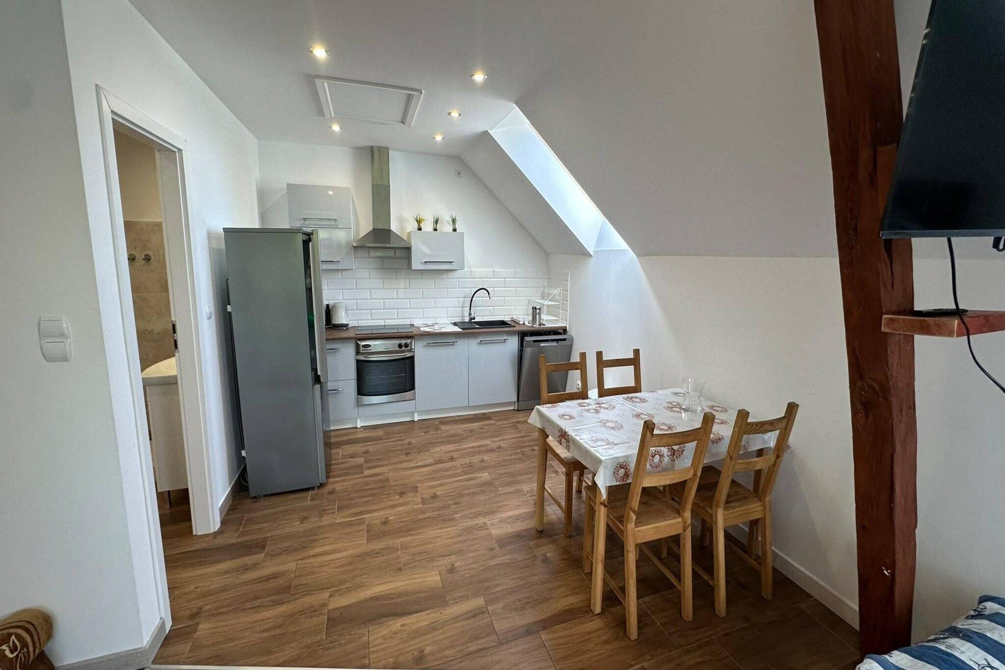 A compact kitchen with modern appliances, a dining area with wooden chairs, and a sloped ceiling with skylight.