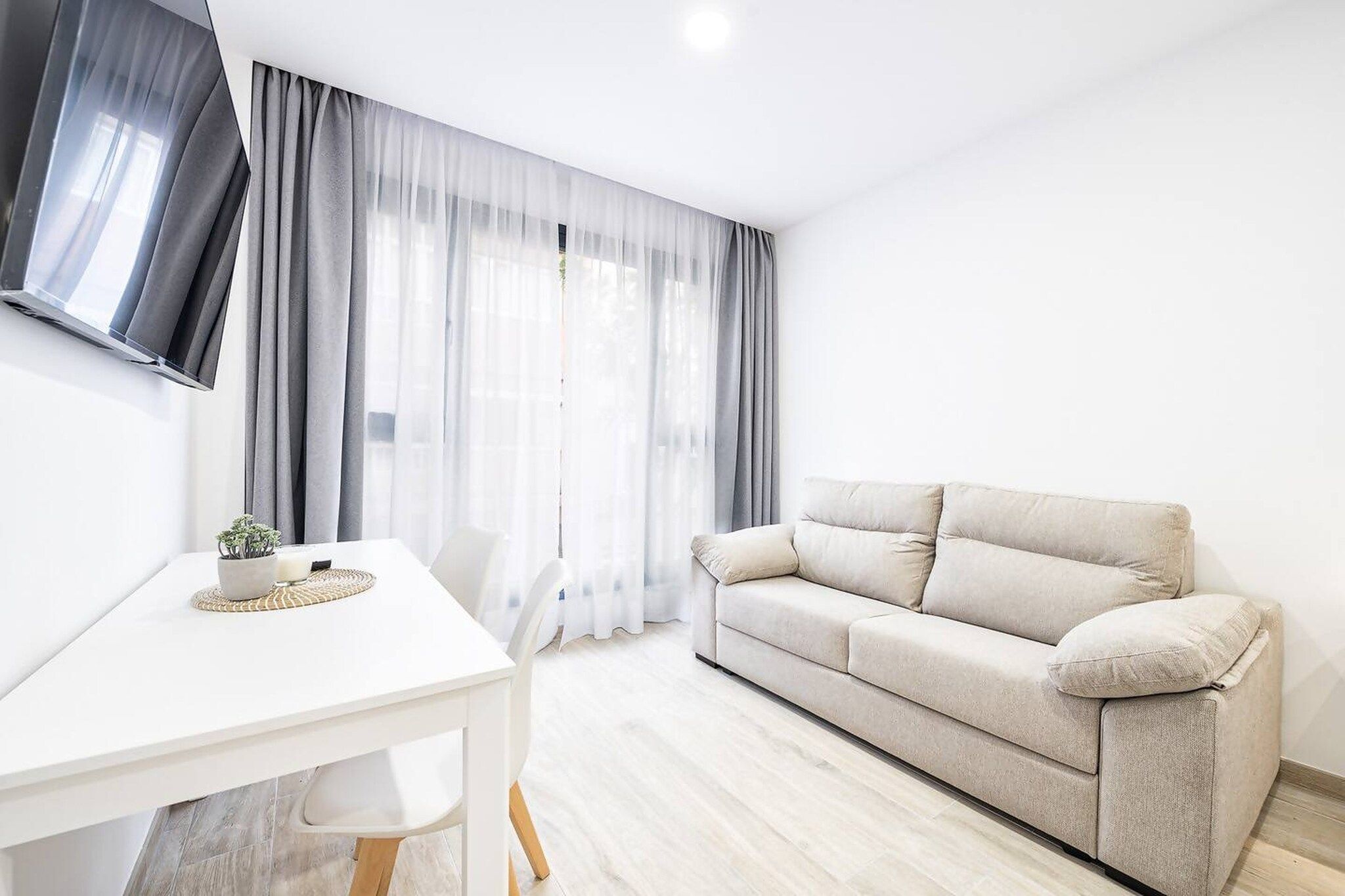 A minimalist living room with a white sofa, a dining table, and sheer curtains.