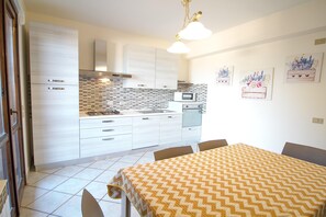 Cozinha moderna com armários brancos, fogão a gás e micro-ondas. Possui uma área de refeições com mesa e cadeiras.