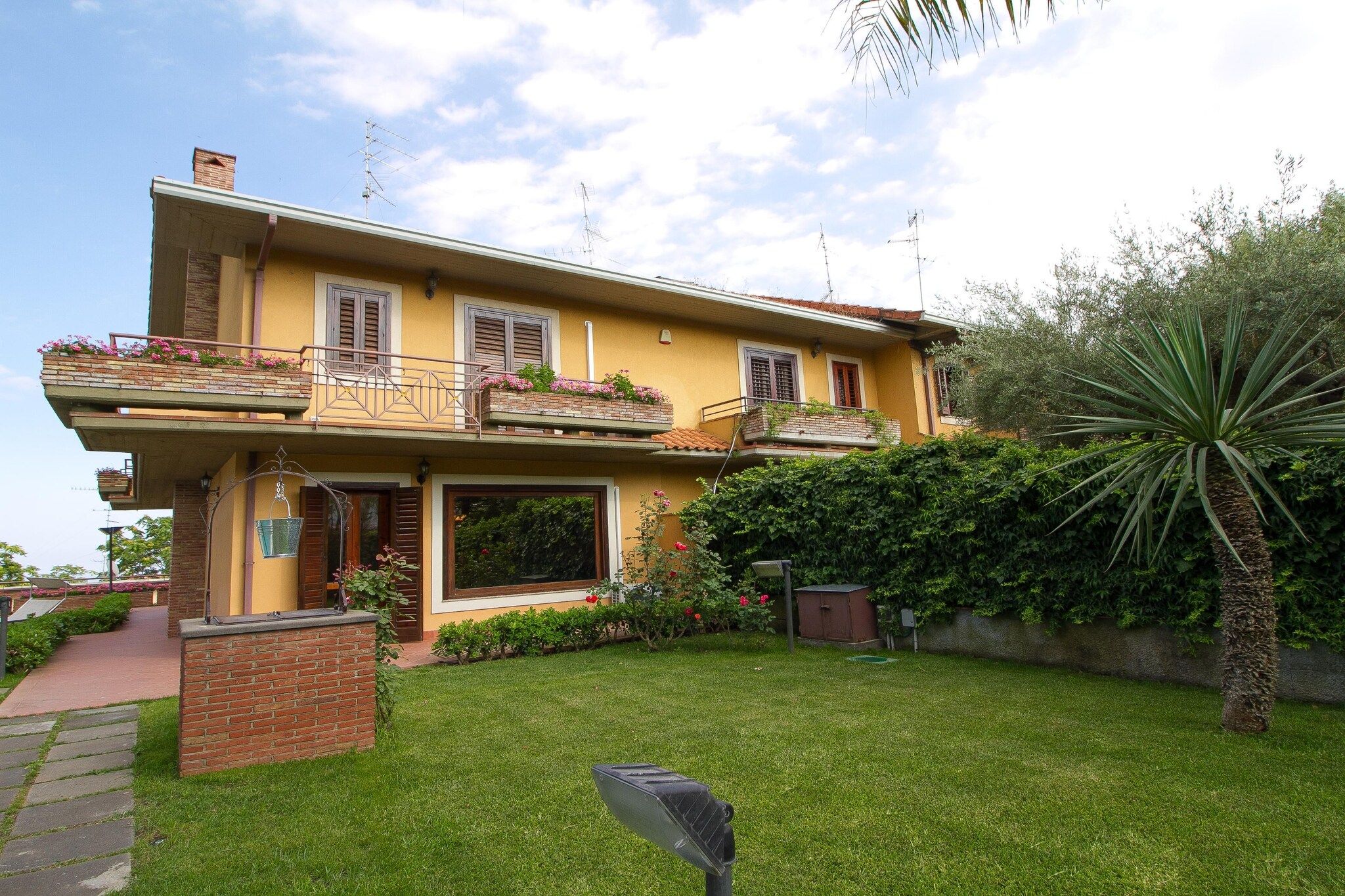 A two-story house with a balcony, a garden, and a palm tree.