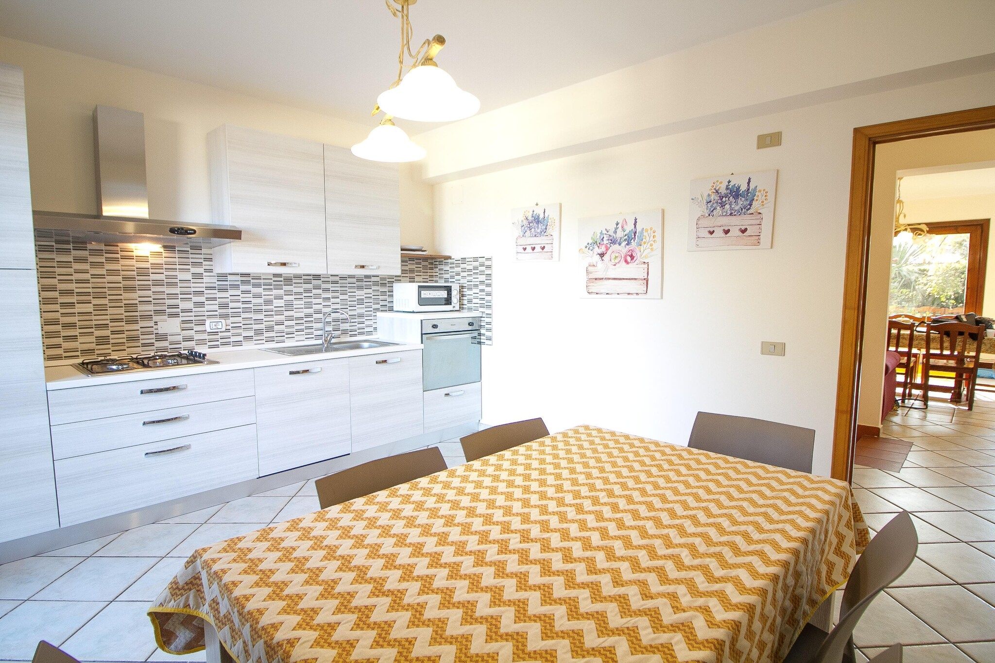 A modern kitchen with white cabinetry, a microwave, stove, and a dining area with a patterned tablecloth.