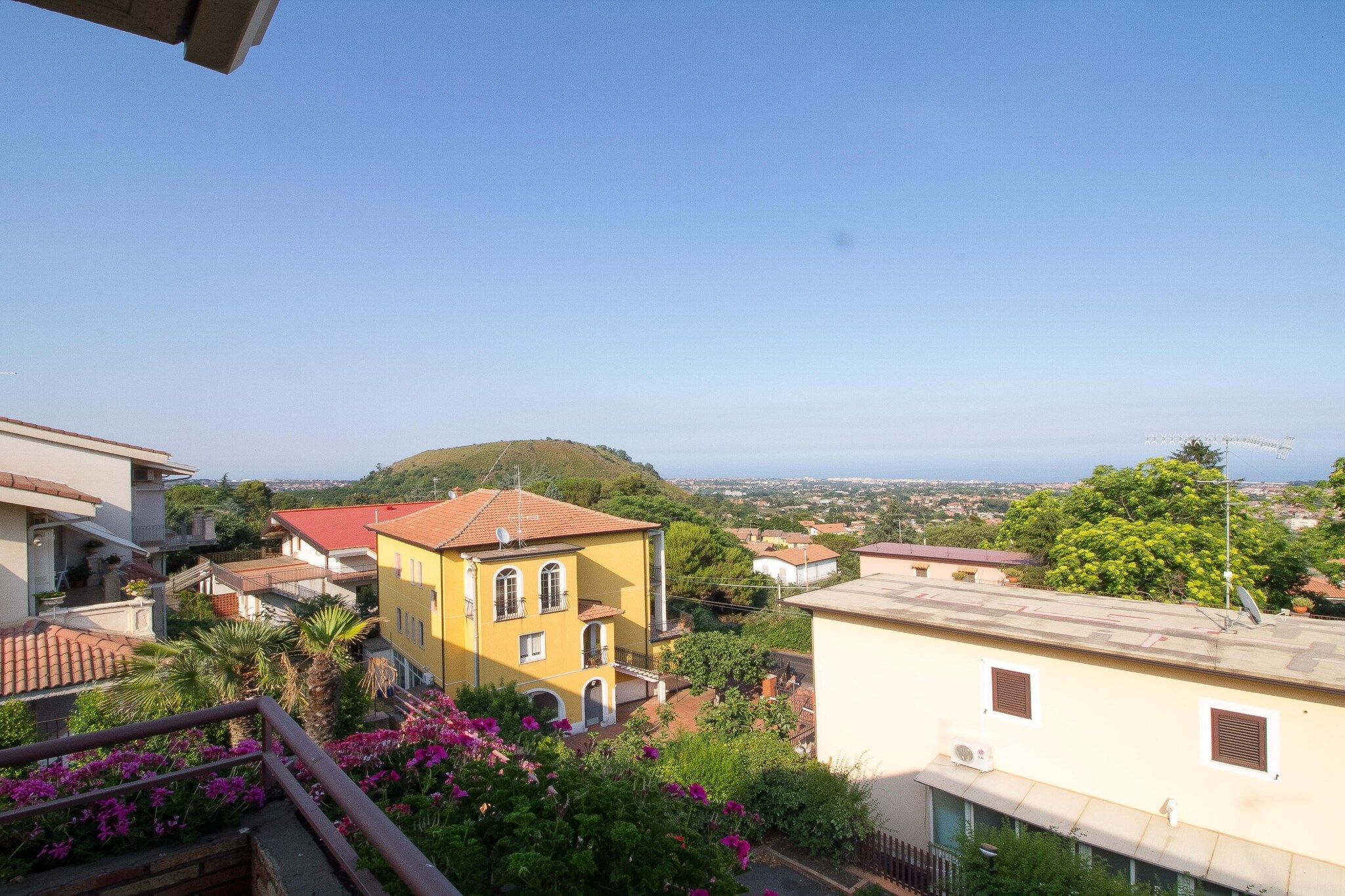 A residential area with buildings, a hill in the background, and a clear sky.
