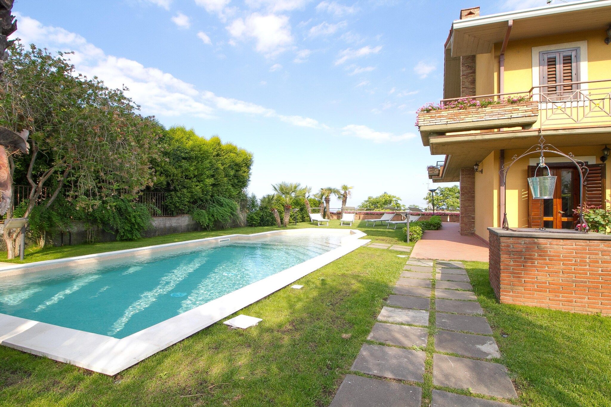 A swimming pool with a paved deck, surrounded by a well-maintained lawn and trees.