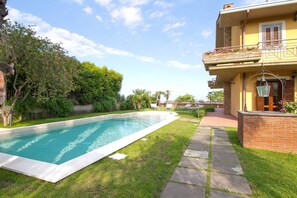 Piscina com deck pavimentado, cercada por gramado bem cuidado e árvores.