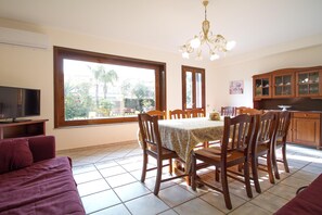 A dining area with a table, chairs, a television, and a view of the outdoors.