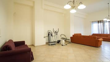 Ein geräumiges Wohnzimmer mit einer großen Sofagarnitur, Trainingsgeräten und einem Kronleuchter.