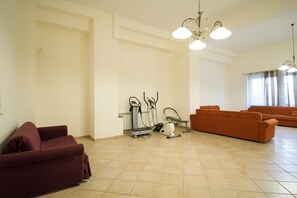 Ampla sala de estar com um amplo sofá, equipamentos de ginástica e um candelabro.