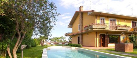 A residential property with a swimming pool, a well-maintained lawn, and a two-story house with a balcony.