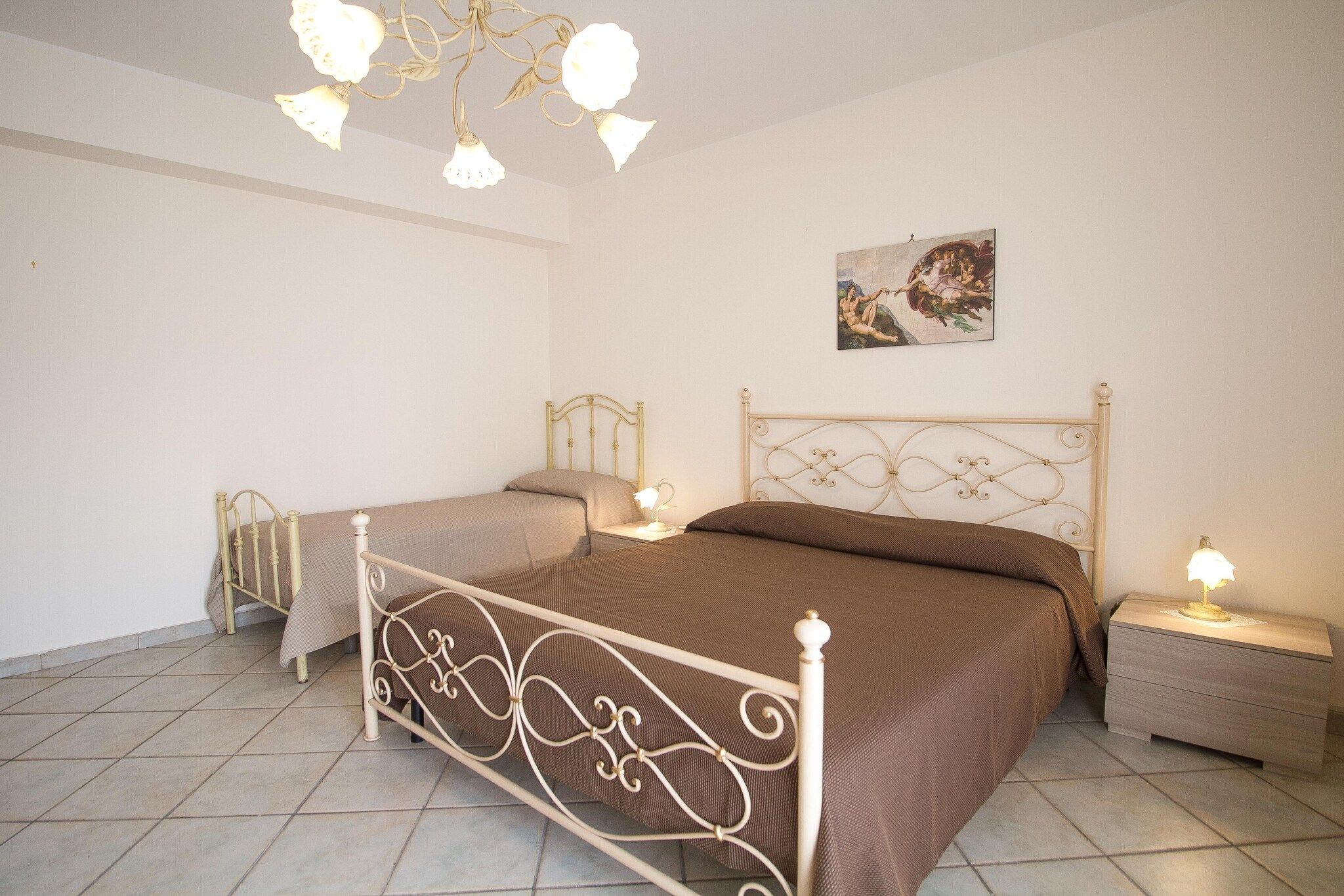 A bedroom with two beds, a chandelier, bedside lamps, and a painting on the wall.