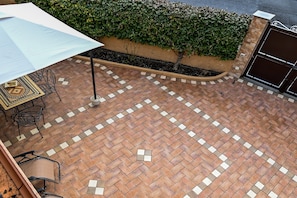 A patio area with a tiled floor, outdoor furniture, and a hedge.