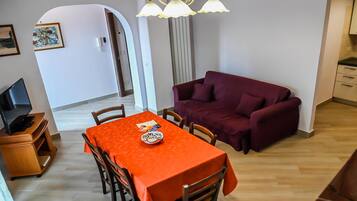 A dining area with a table set for two, a purple sofa, and a TV on a stand.