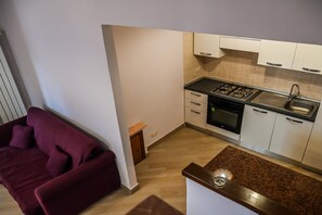 Una cocina compacta con estufa, horno y pileta, junto a una sala de estar con sofá.