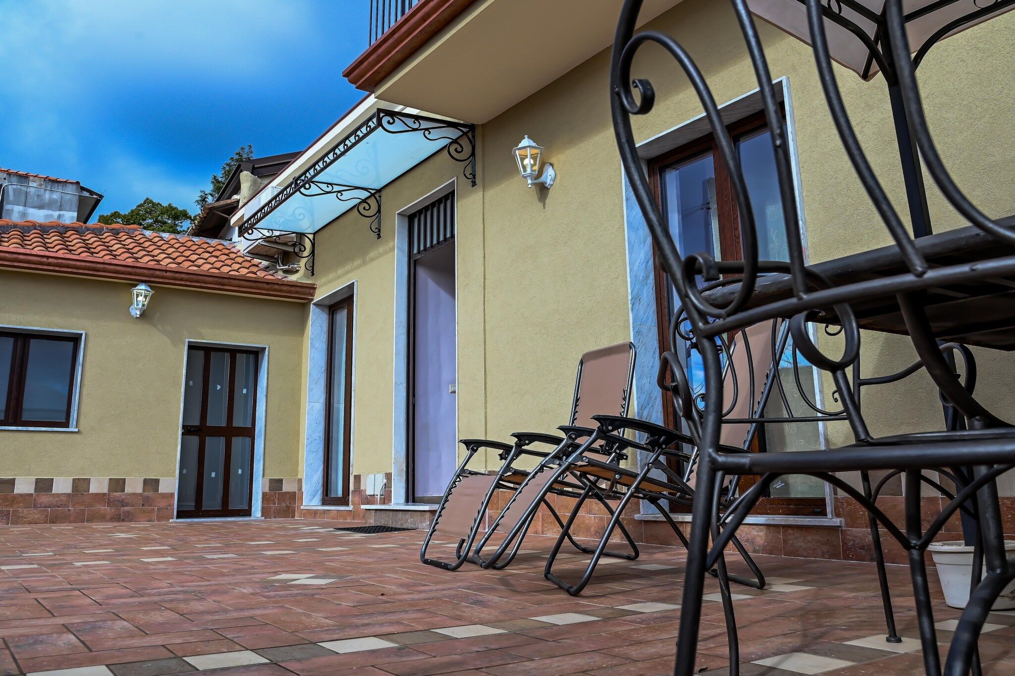A patio area with outdoor furniture and a building with a tiled roof and multiple windows.
