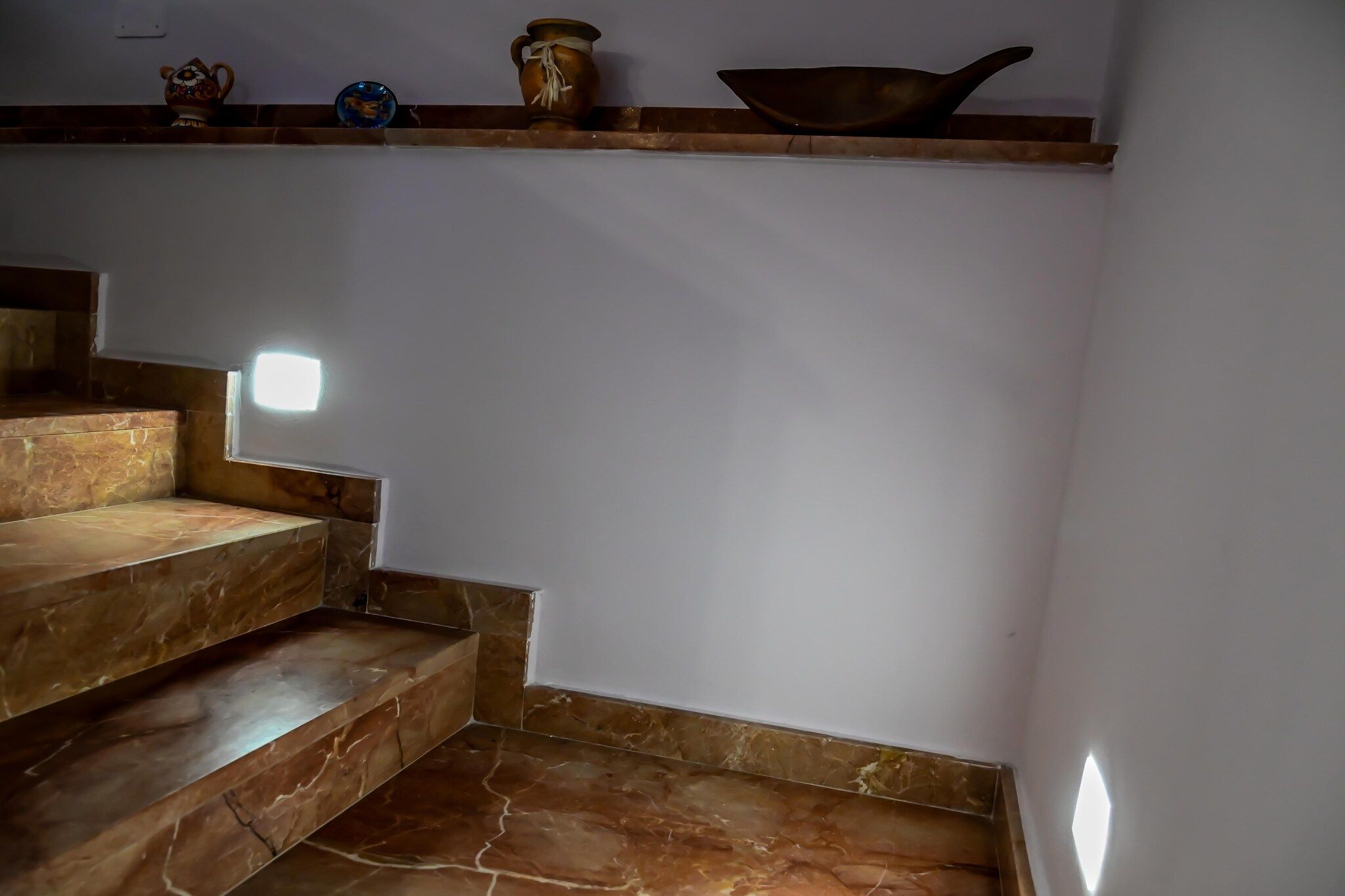 Eine Treppe mit Marmorverkleidung, die zu einer Zwischenebene führt, auf der sich eine Ablage mit Dekoration befindet.