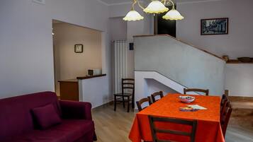 A dining area with a table set for four, a staircase, and a living room with a sofa.