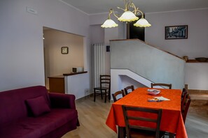 Un comedor con una mesa dispuesta para cuatro personas, una escalera y una sala de estar con un sofá.