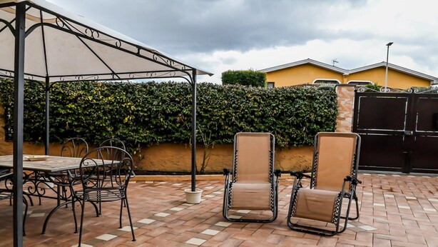 An outdoor patio with a table and chairs, a covered area, and a hedge in the background. - Family Sicilian Heritage Home (TRECASTAGNI)