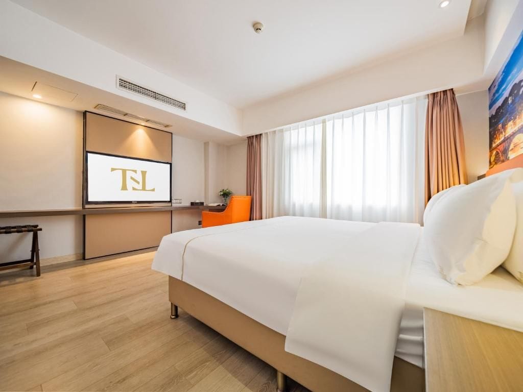 Habitación de hotel con una cama grande, un escritorio con computadora y un televisor mostrando 'TL'.