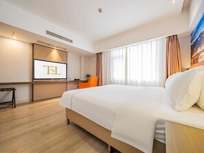 Habitación de hotel con una cama grande, un escritorio con computadora y un televisor mostrando 'TL'.