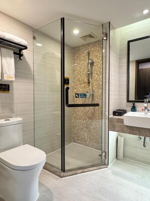 Un baño moderno con ducha envuelta en vidrio, inodoro blanco y lavabo con espejo sobre él.