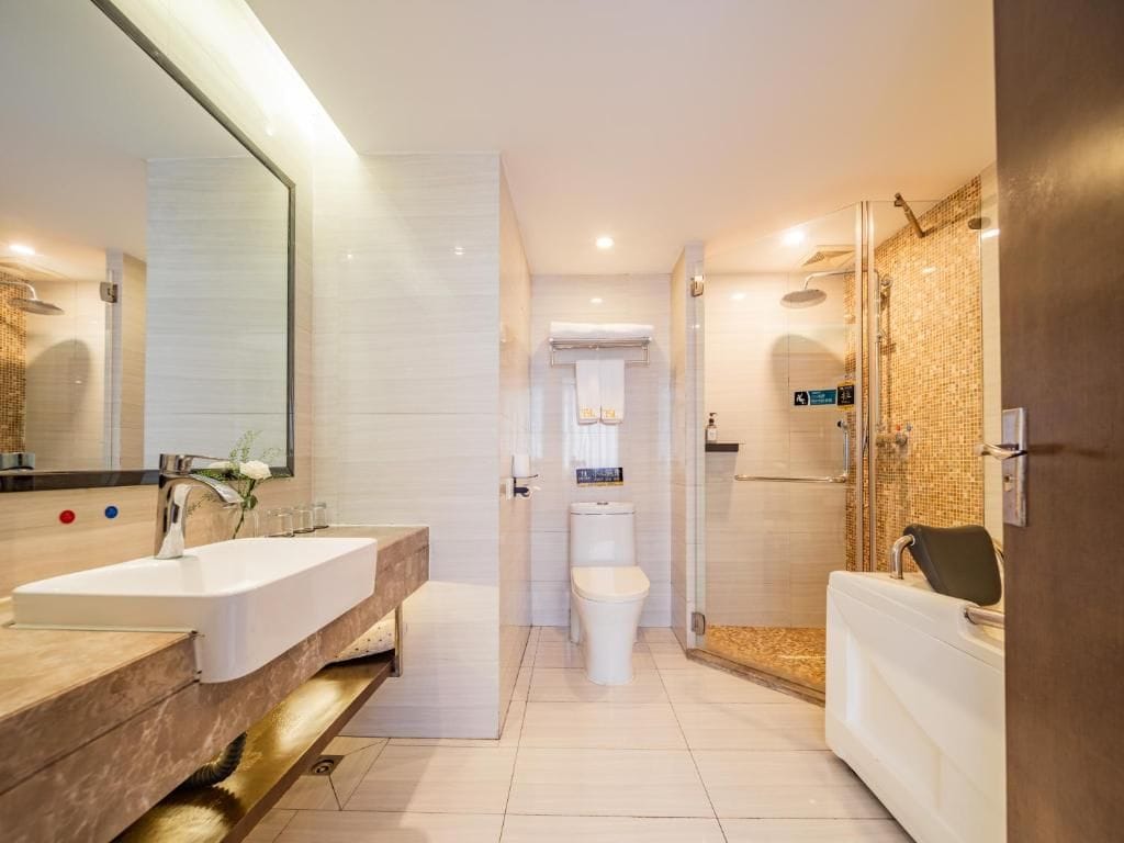 Un baño moderno con un espejo grande, un lavamanos, un inodoro y una zona de ducha.