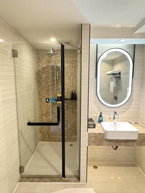Un baño moderno con ducha envuelta en vidrio, espejo redondo y lavamanos blanco.