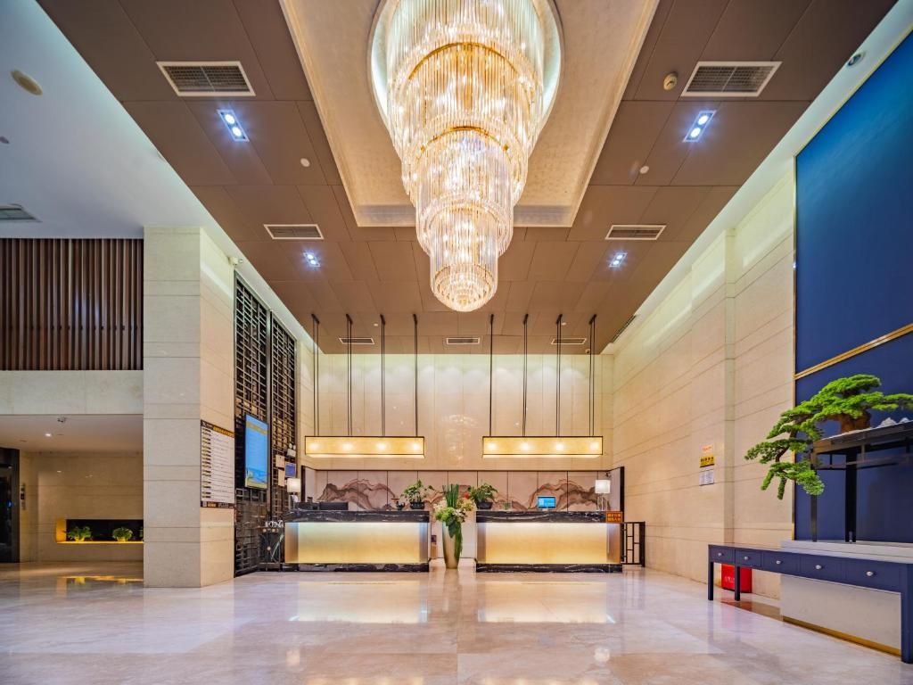 A hotel lobby with a reception desk, a large chandelier, and a modern design.