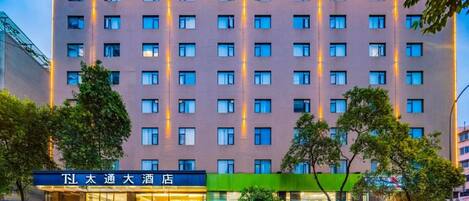 A multi-story hotel with a row of windows on each floor, a ground-level entrance with a sign, and a green awning over the entrance.