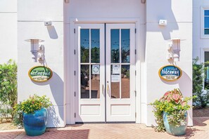 A building entrance with a double door, two potted plants, and two signs indicating 'The Village Meeting Place' and 'Hideaway.' - 🌴Dune's Perch: Beach Club Resort with Pool + Hot Tub + On-Site Dining (Gulf Shores)