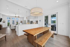 A spacious kitchen with a wooden dining table and bench, white cabinetry, and a large pendant light. - 🌴Dune's Perch: Beach Club Resort with Pool + Hot Tub + On-Site Dining (Gulf Shores)