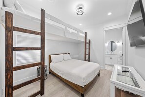 A bedroom with a bunk bed, a bedside table, a mirror, and a TV. - 🌴Dune's Perch: Beach Club Resort with Pool + Hot Tub + On-Site Dining (Gulf Shores)