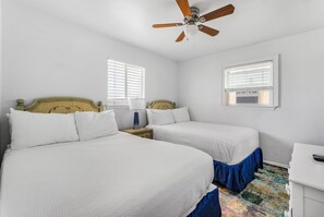 Une chambre avec deux lits, un ventilateur de plafond et deux fenêtres équipées de stores.